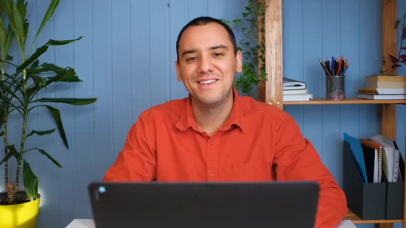 Portrait of Happy Young Businessman Sitting at Table in Home Office and Working at Laptop