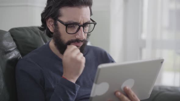 Close-up Face of Confident Caucasian Man in Eyeglasses Rubbing His Black Curly Beard As Thinking