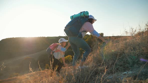 Mother and Daughter with Backpacks Running Through the Meadow at Sunset. Family Tourism Concept.