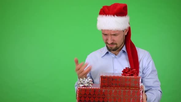 A Young Handsome Man in a Christmas Hat Holds Presents and Acts Disappointed - Green Screen Studio