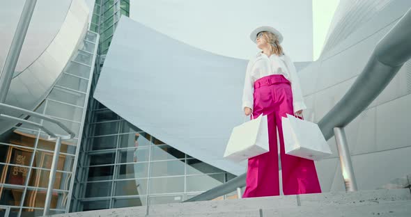 Woman in Stylish Clothes with White Shopping Bags Posing at Shopping Mall, 