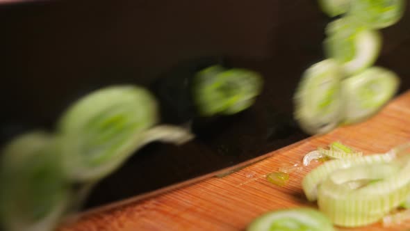 Macro cutting spring onions with a black knife on a wooden chopping board.