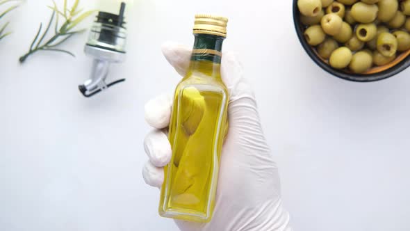 Holding Bottle of Olive Oil and Fresh Olive in a Container on White