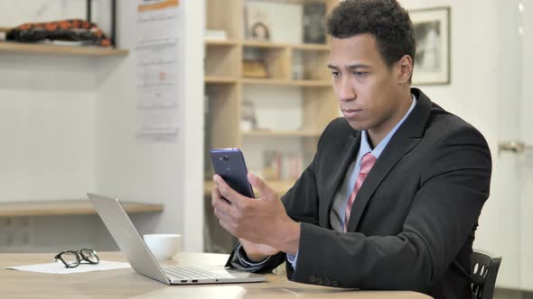 African Businessman Using Phone and Laptop for Information