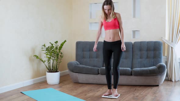 Distressed Woman in Sportswear Measures Her Weight on the Floor Scales