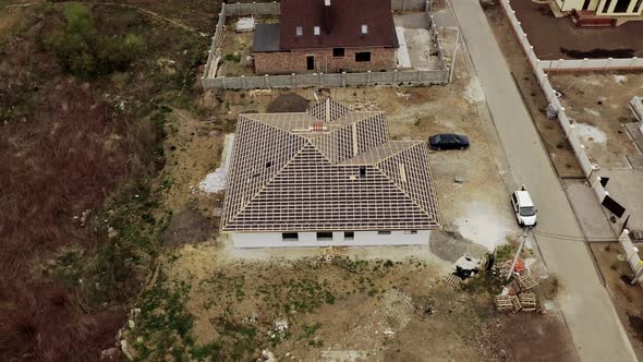Aerial view of unfinished brick house with wooden roof frame structure under construction. 