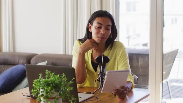 Mixed race gender fluid person recording a podcast using laptop reading notes at home