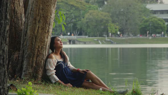 Transgender Asian Woman Leaning Against a Tree in the Park Enjoying the Moment