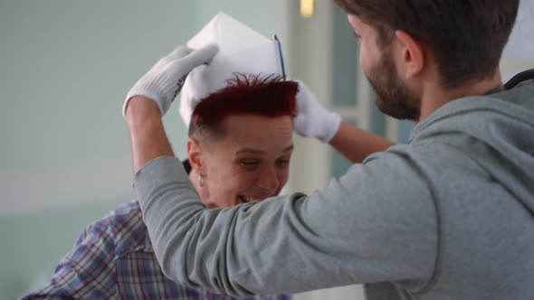 Redhead Woman Laughing Talking As Man Putting on Paper Hat