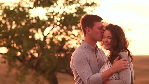 Portrait of a Happy Pregnant Couple in a Field at Sunset with Red Sunlight