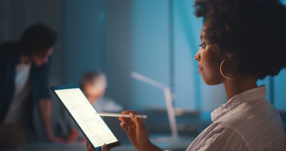 Professional Afroamerican Architect Studying Blueprint on Digital Tablet in Office Working Late