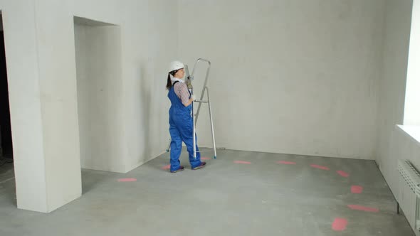 Repairwoman with Ladder Inspects Room to Renovate