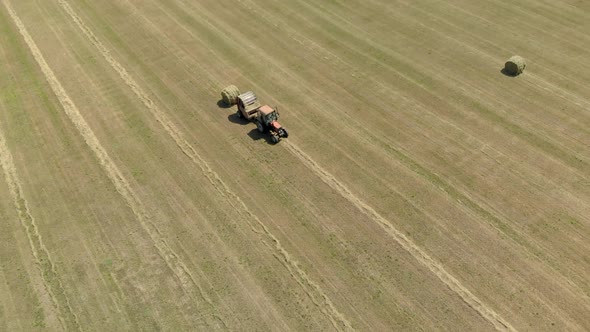 Aerial: Farmer on a Tractor Baling and Wrapping Hay Rolls in a Meadow in Hot Sunny Weather