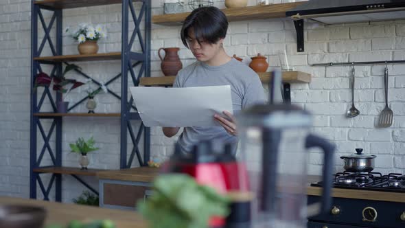 Serious Man Writing on Paper Standing in Kitchen Indoors