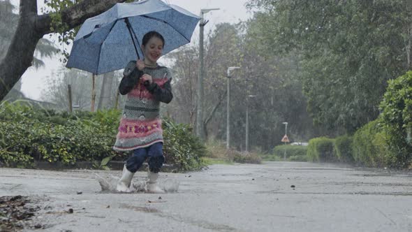 Slow motion of a little girl skipping in puddles holding an umbrella in the rain