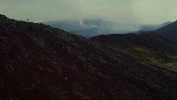 Person On The Hill Watching Volcanic Eruption With Fiery Lava Spewing Out Of Crater At Dusk. drone f