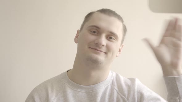 Young Brunette Man Waving Hello at Camera and Smiling. Portrait of Cheerful Caucasian Guy Greeting