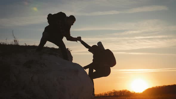 Silhouette of Helping Hand Between Two Climber. Two Hikers on Top of the Mountain, a Man Helps a