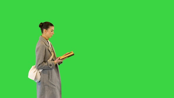 Young Woman in Stylish Clothes Walks with a Book Stops and Closes It on a Green Screen Chroma Key