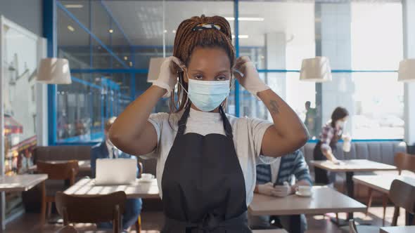 African Waitress Wearing Protective Mask and Gloves Standing in Cafe During Covid-19 Preventing.