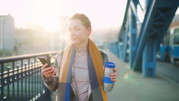 Caucasian Businesswoman in a Coat Walking Across the Bridge on a Frosty Morning Drinking Coffee and