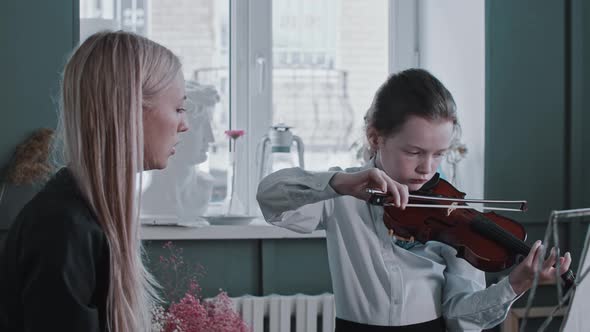 A Girl Playing Violin During Lesson with Blonde Woman Teacher  Telling to Hold the Bow Another Way