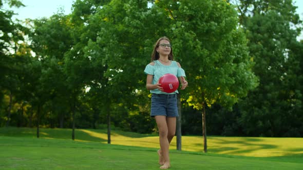 Happy Girl Standing in Green Field. Pretty Girl Holding Ball in Hands