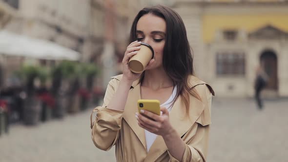 Young Attractive Girl Drinking Coffe Laughing Using Her Smartphone and Typing Standing at City