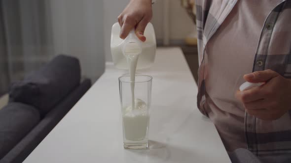 Unrecognizable Woman Pouring Glass of Milk From Plastic Bottle Indoors