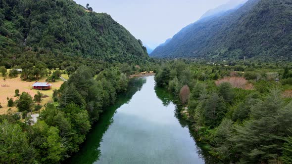 Dolly out aerial view of the Cochamo River and Cochamo Valley with mountains in the background.