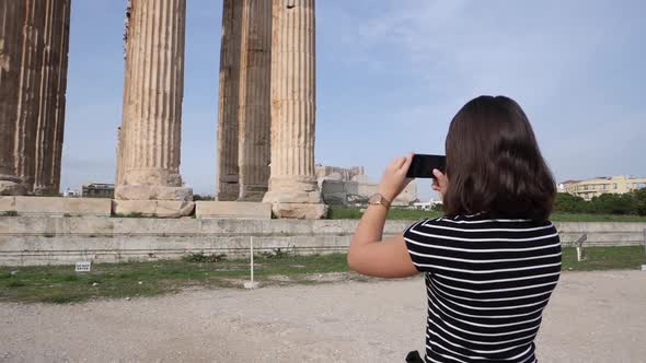 A young woman is filming an old roman building with her smartphone.