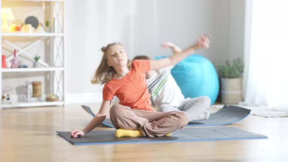 Cute Caucasian Girl and Blurred Boy Doing Sport Exercises Sitting on Exercise Mat at Home