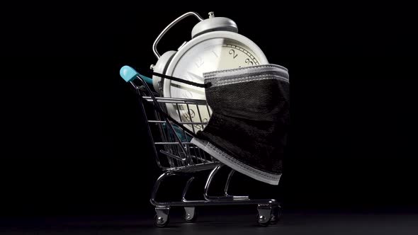 Vintage analog clock in a shopping cart with a medical protective mask on a shiny metal basket.