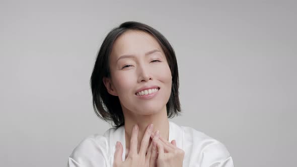 Happy Asian Woman Touching Face Stroking Cheeks Over Gray Background