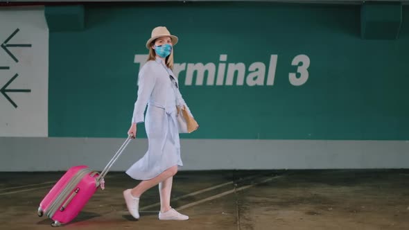 Stylish Woman in Colorful Face Mask Walking By Airport Parking with Suitcase