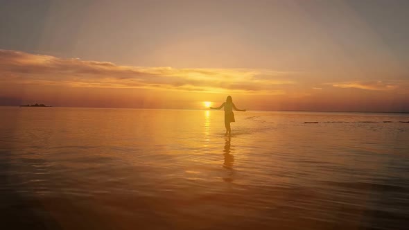 Brunette Woman in a Dress Running Along Water at Sunset or Sunrise