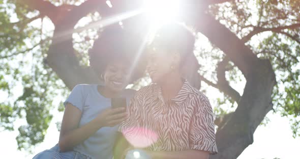 Two mixed race women look at smartphone in park