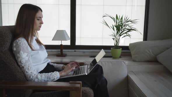 The Beautiful Woman Working On Laptop. Near Big Windows And A Flower In A Pot