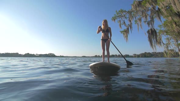 Slow motion shot of young woman sup stand-up paddleboarding on a lake.