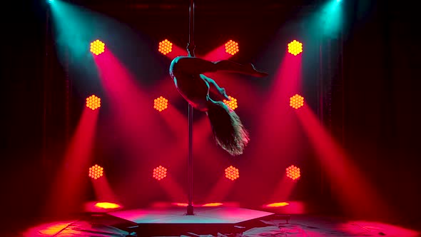 A Young Slender Woman Rotates on a Pole Upside Down. Dark Studio with Red Spotlights. A Female