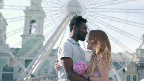 Young Interracial Couple Hugging Near Ferris Wheel in the City