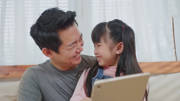 Asian loving father with little girl using tablet learning from home and playing internet online. alt