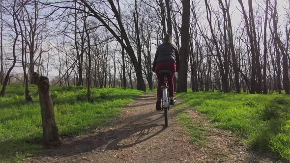 Young Woman on a Bicycle Rides Along a Path in the Forest in a Sunny Spring Day