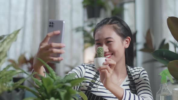 Close Up Of Smiling Asian Woman Holding Cactus Plant And Taking Photo By Smartphone At Home