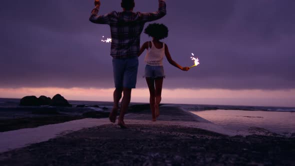 Couple running with sparklers on concrete pier at beach 4k