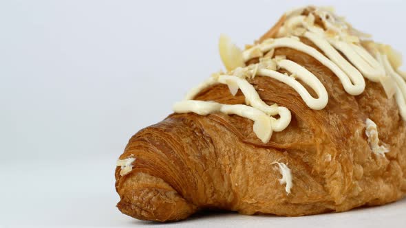 Rotation of a baked croissant with cream and almonds on a white plate.