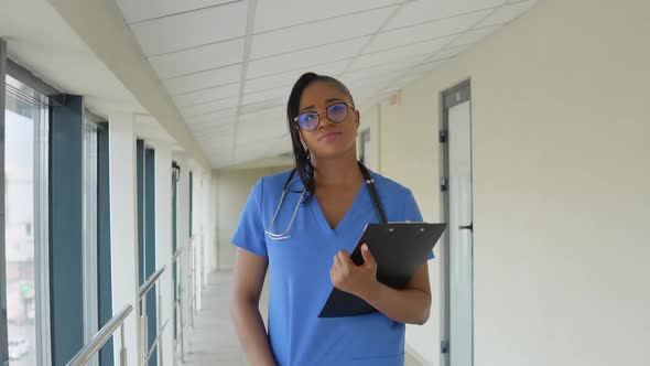 Young African American Doctor Woman in a Blue Suit Walks Along the Corridor of the Clinic with