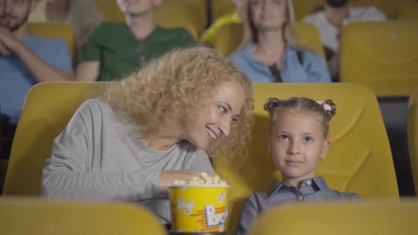 Embarrassed Caucasian Mother Closing Daughter's Eyes in Cinema. Portrait of Relaxed Parent and Child