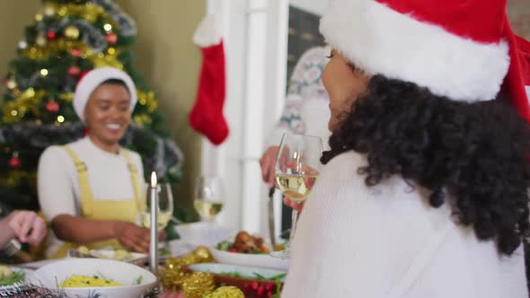 Happy mixed race woman in santa hat celebrating meal with friends at christmas time