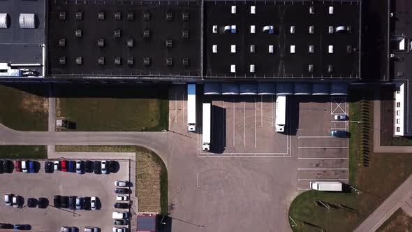 Zoom Out Aerial Shot of Industrial Warehouse/ Storage Building/ Loading Area where Many Trucks Are L